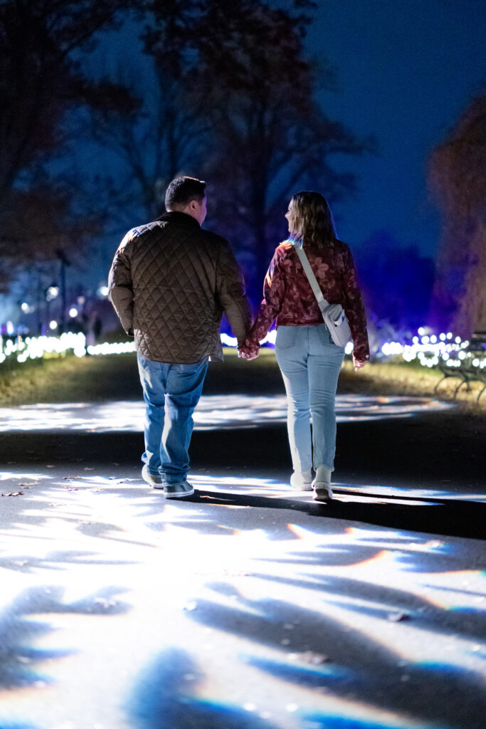 Couple walking away with giant snowflake projections underfoot during nighttime proposal shoot