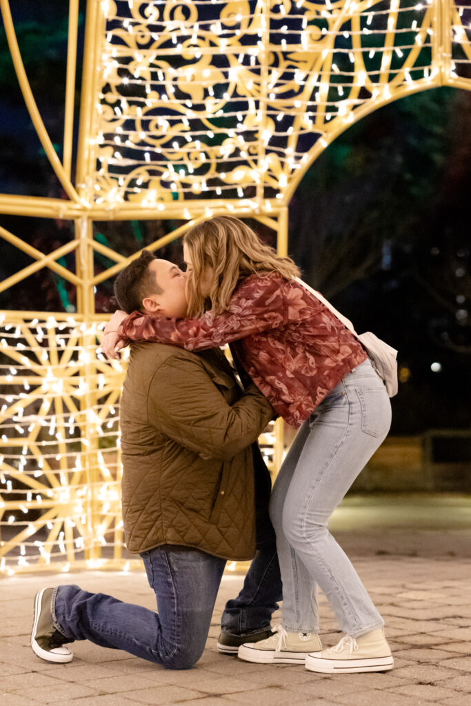 Bride-to-be bending down to kiss fiancé during proposal, joyful and spontaneous