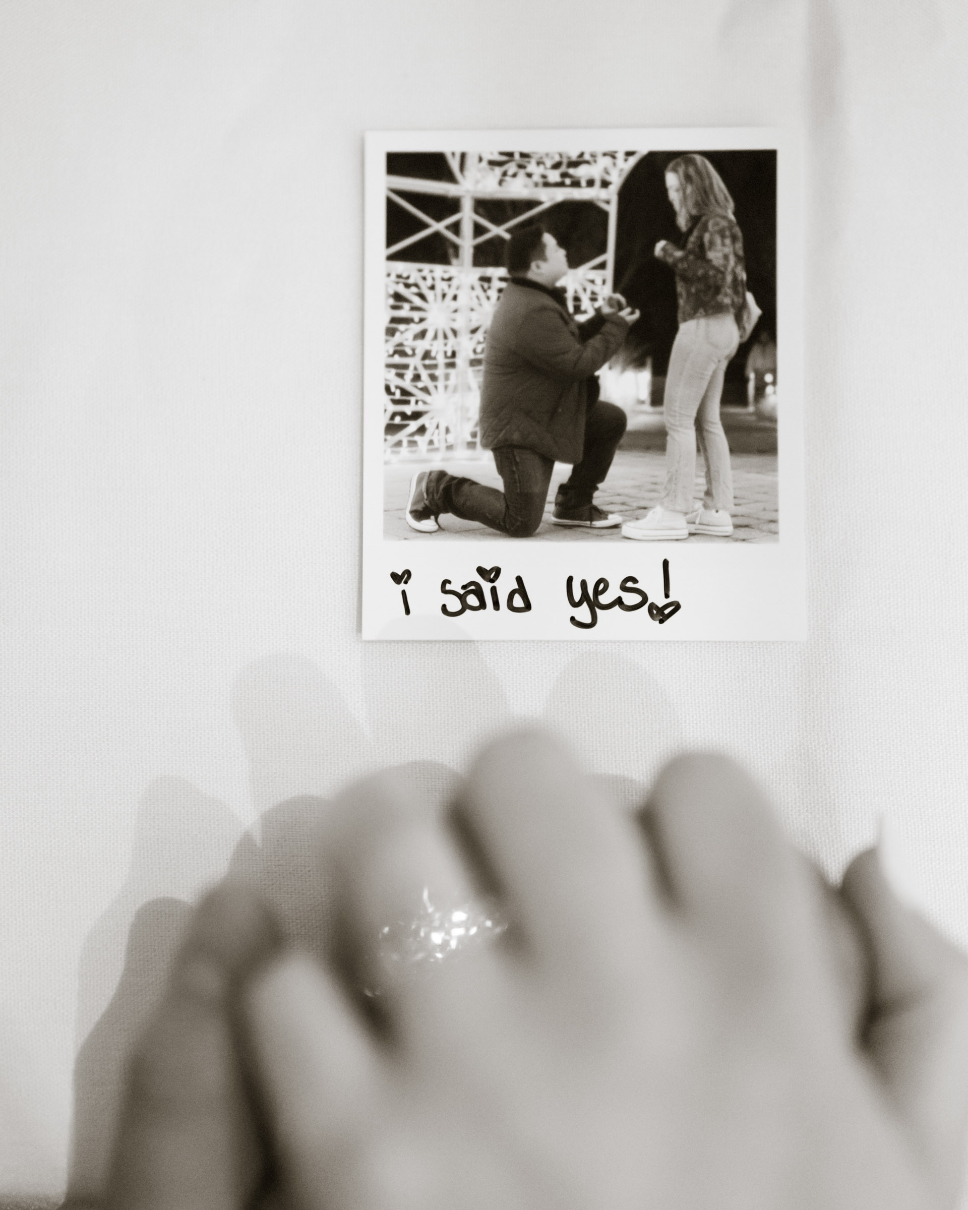 Black and white photo of Polaroid on tablecloth with handwritten “I said yes!” and heart accents