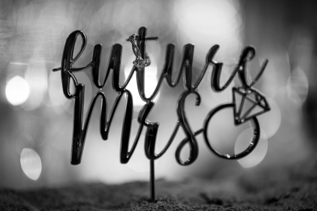 Black and white detail of engagement ring hanging from the T in “Future Mrs” dessert lettering
