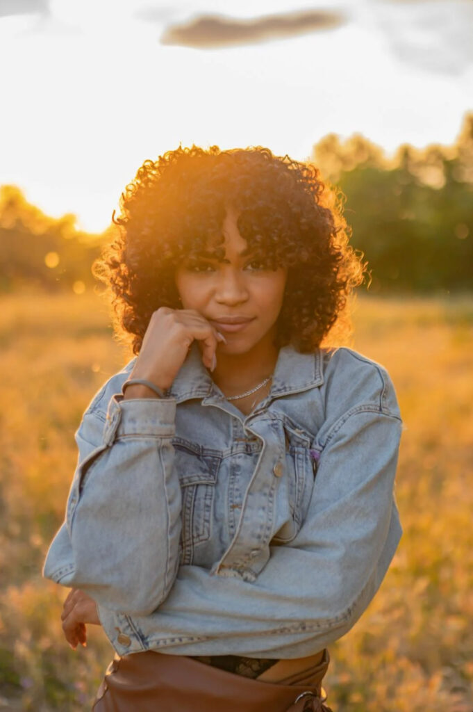 Woman in denim jacket in open field during golden hour with sun backlighting her hair