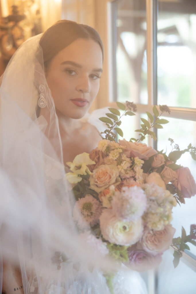 Bride gazing through her veil near a softly lit window before the wedding ceremony
