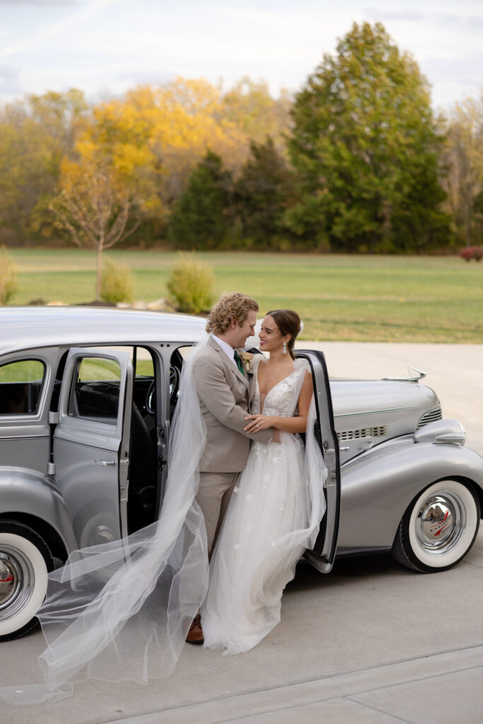 Bride and groom posing in front of a vintage car and elegant wedding venue