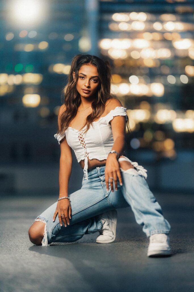 Woman crouching in a city parking lot at night lit by flash with office lights in the background