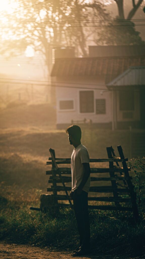 Man in white shirt and jeans looking down a dirt road at sunrise with golden glow in the countryside
